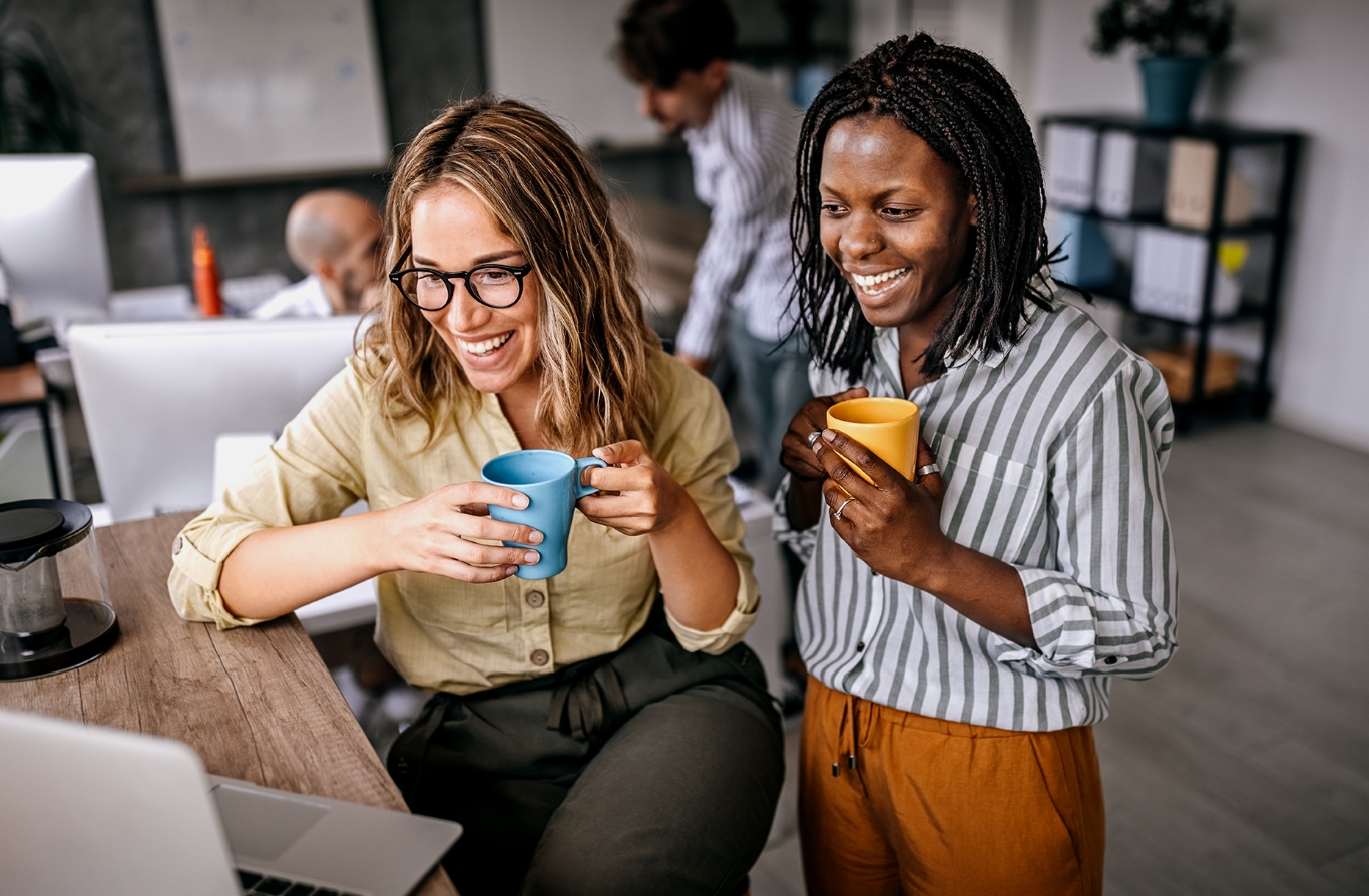 Two co-workers sitting in an office setting, smiling